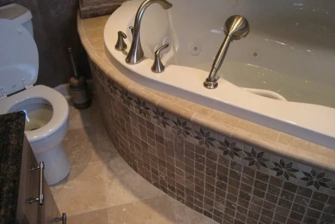 Corner tub with a brown granite deck and tiled apron