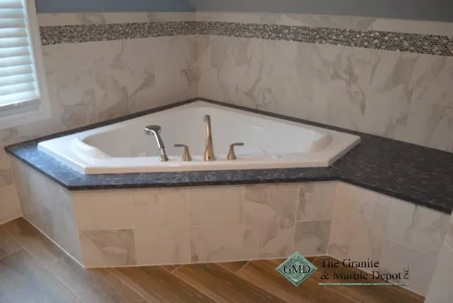 Corner tub with a grey granite deck and mosaic tile band
