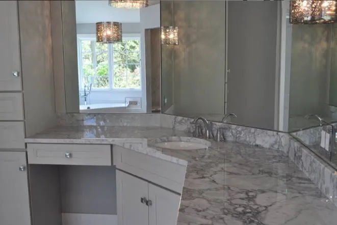 Grey marble vanity with a seated makeup station and glass shower beyond