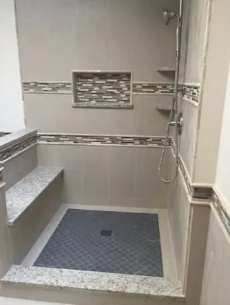 Grey tiled shower with a glass mosaic band and a stone bench