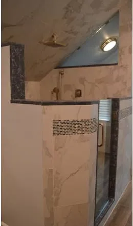 Marble shower walls with gold fixtures and a mosaic tile band