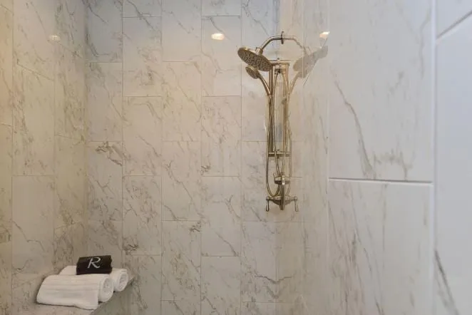 Marble shower wall with chrome fixtures and a corner shelf