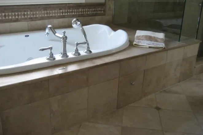 Marble tub deck with a bridge faucet beside a glass shower enclosure