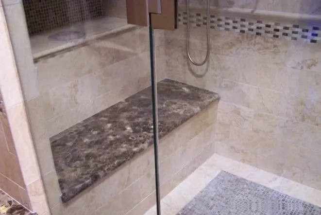 Walk-in shower with a granite bench and mosaic tile band