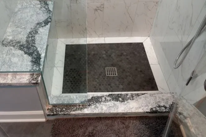 Shower floor in dark stone with a granite curb and marble walls