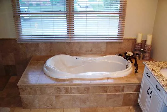 Travertine tub deck beside a granite vanity in a warm-toned bathroom
