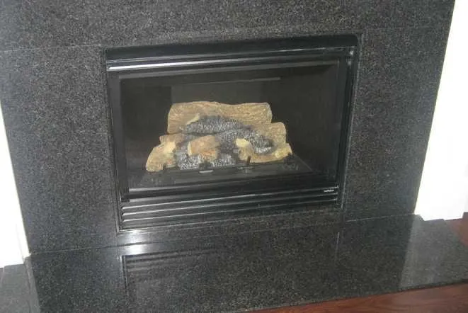 Black granite fireplace surround around a gas log insert