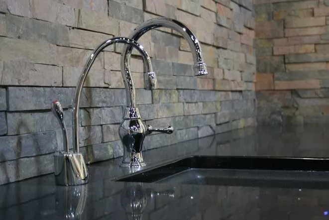 Polished black granite counter against a stacked stone backsplash with a tall gooseneck faucet