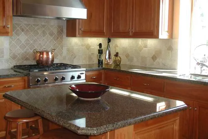 Brown granite peninsula with bar seating beneath a travertine tile backsplash and range hood