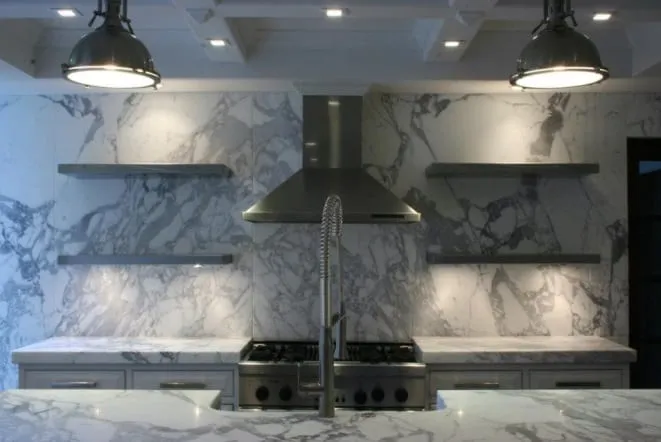 Full-height white marble backsplash with bold grey veining behind a professional range