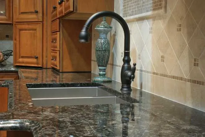 Close-up of a dark granite countertop meeting a travertine tile backsplash