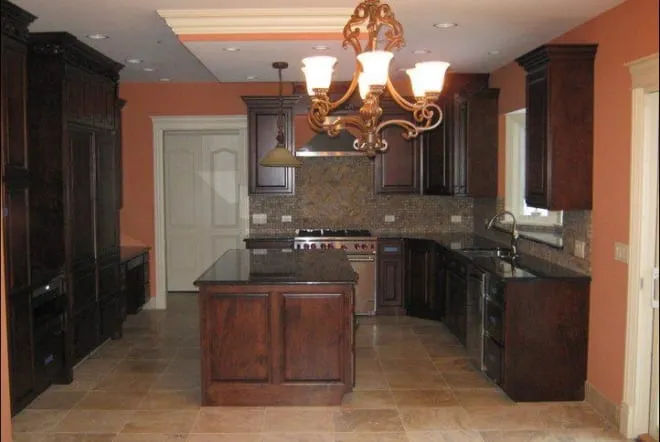 Dark cabinets and dark granite island lit by a wrought-iron chandelier