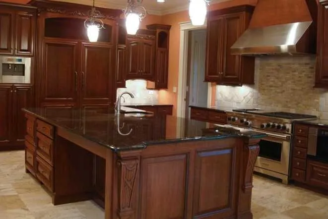 Long dark granite island in a cherry-cabinet kitchen with pendant lighting