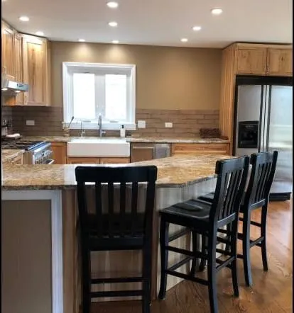Gold granite counter with a farmhouse apron sink and black bar chairs