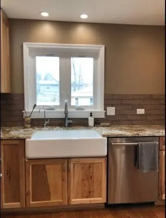 Farmhouse apron sink set into a gold granite countertop beneath a window