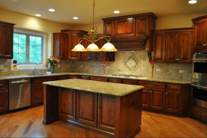 Gold granite island beneath a chandelier in a cherry-cabinet kitchen