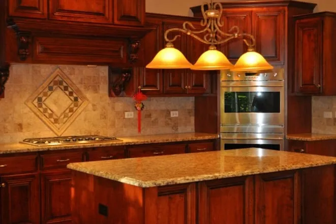Gold granite counters with an ornate tile backsplash in a cherry-cabinet kitchen