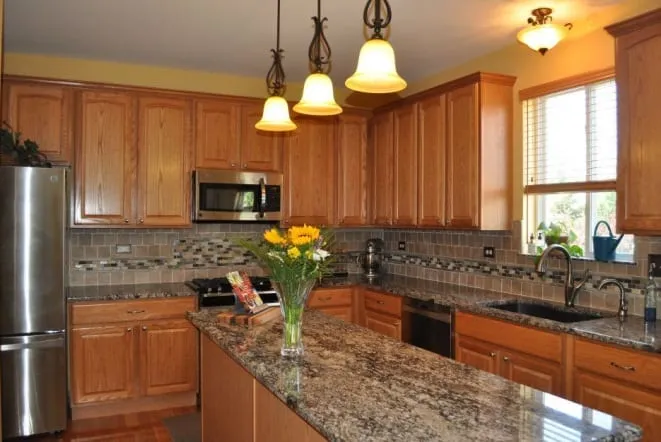 Granite countertops and tile backsplash in an oak kitchen with pendant lights
