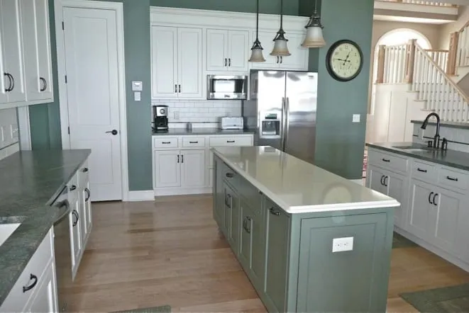 Sage green island with grey stone counters and a white subway tile backsplash