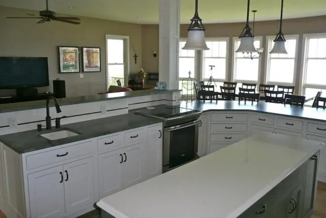 Long kitchen island with dark countertops and white cabinets in a bright open plan