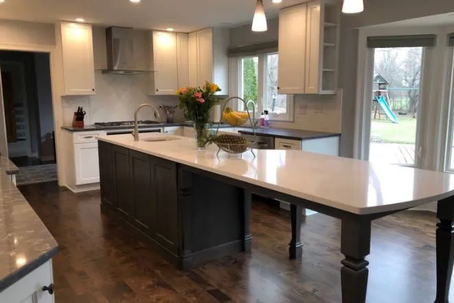 Long dark island with white stone top in a kitchen opening to patio doors