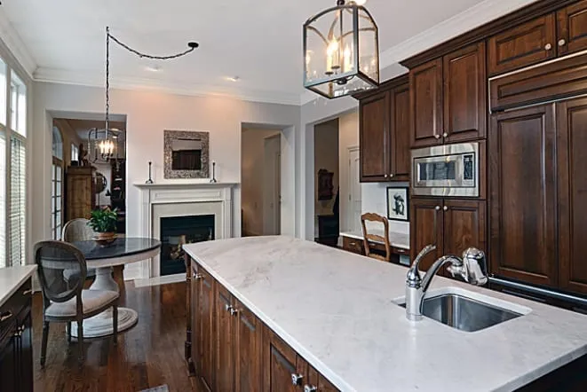White stone island in a dark-cabinet kitchen open to a fireplace