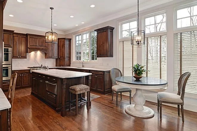 White stone island and a round pedestal table in a dark wood kitchen
