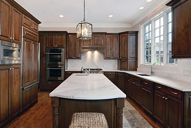 White marble island beneath lantern pendants in a dark wood kitchen