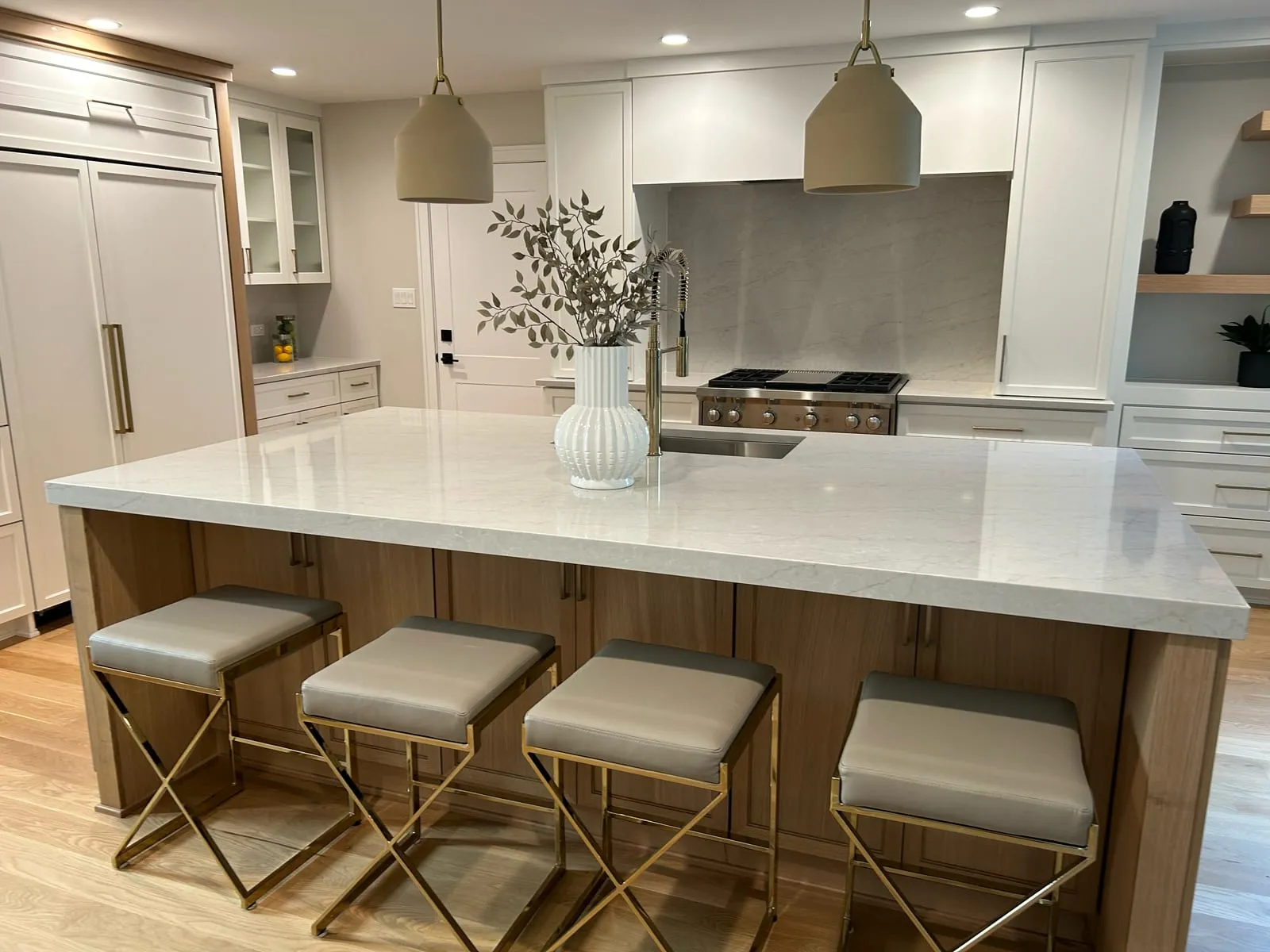 Bright white kitchen with an oversized quartz island, white-oak base and brass counter stools beside a professional range
