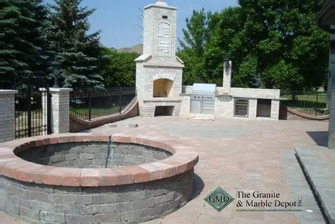 Paver patio with a round fire pit and a tall outdoor stone fireplace